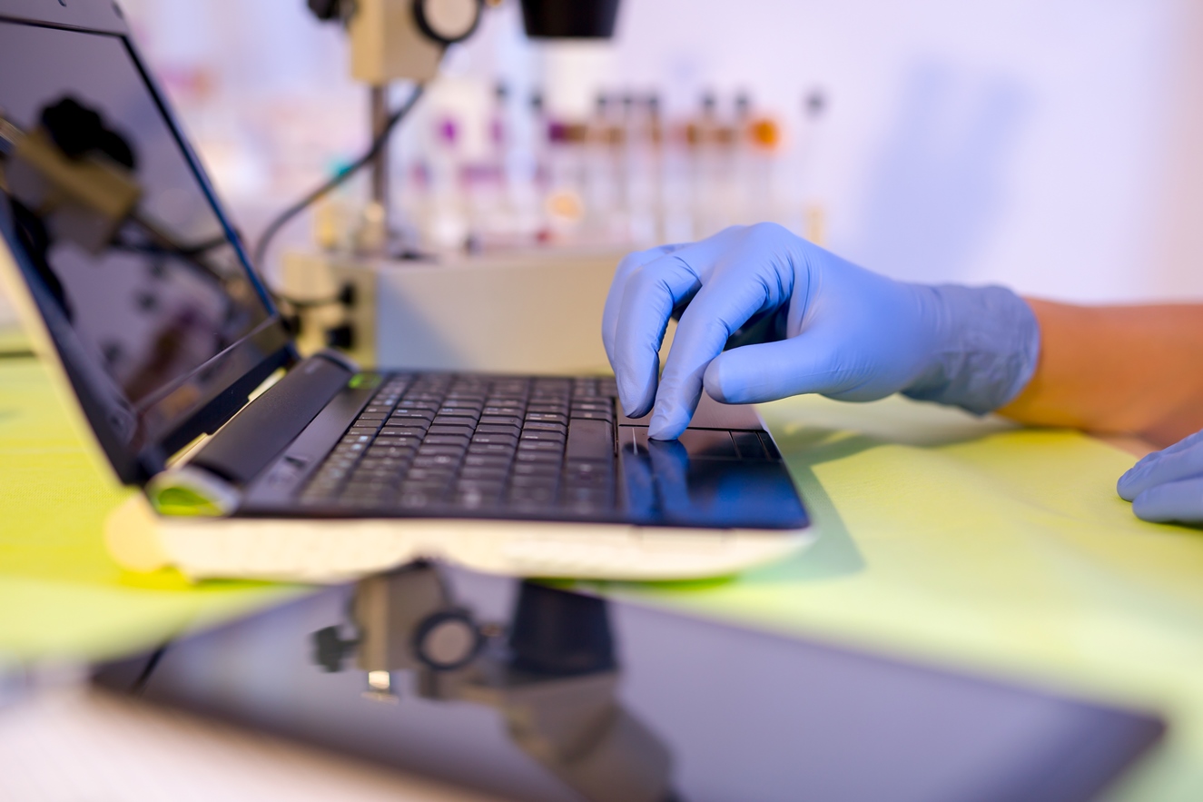 Hands wearing gloves working on a laptop computer.